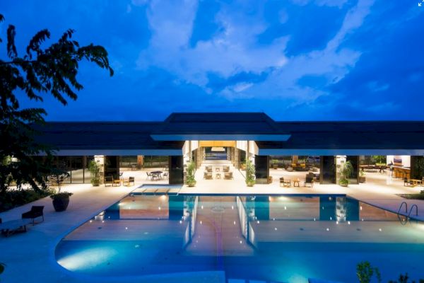 A luxurious poolside view with a modern building, surrounded by lounge chairs and trees, under a dramatic evening sky.