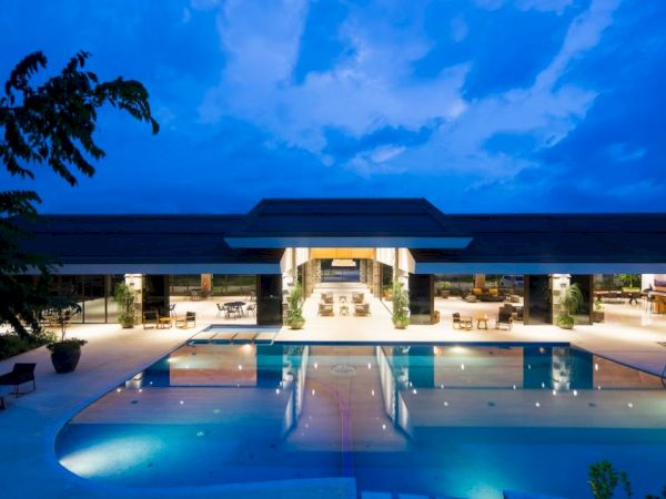 A luxurious poolside view with a modern building, surrounded by lounge chairs and trees, under a dramatic evening sky.