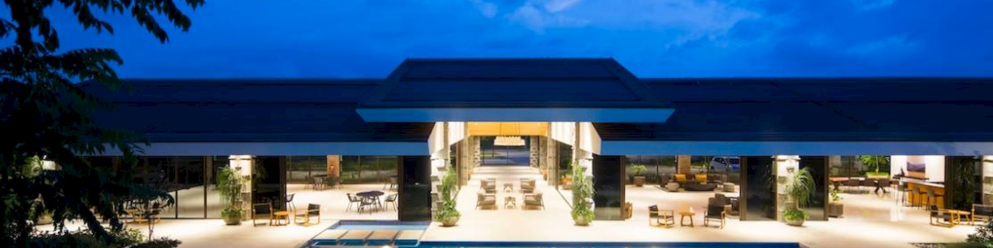 A luxurious building is visible with a large illuminated pool in front, set against a vibrant evening sky.
