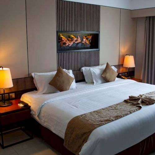 A cozy hotel room with a large bed, bedside tables, lamps, folded towels, and a window covered by curtains.