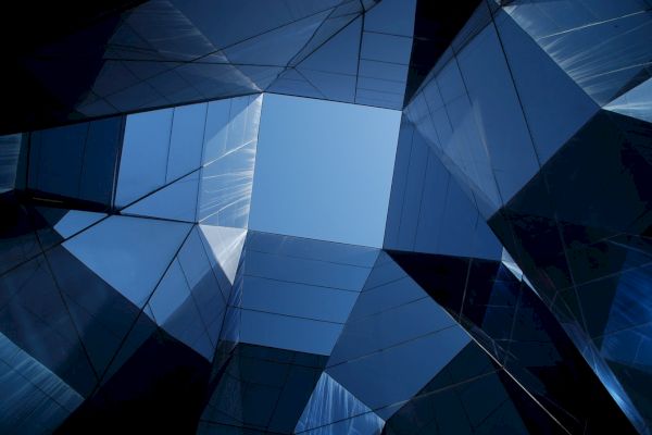 Looking up at a geometric glass structure forming a symmetrical view, reflecting the blue sky.