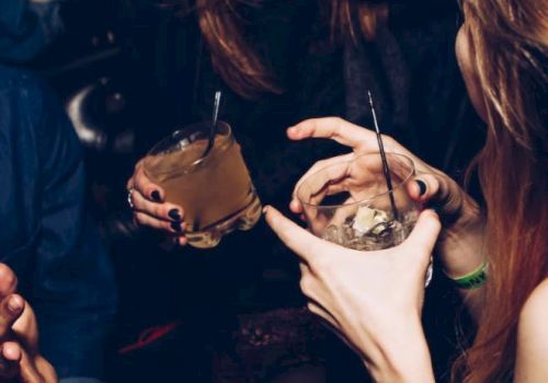 People enjoying drinks and laughing, holding cocktails with straws in a lively social setting.