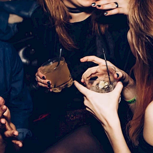 People enjoying drinks and laughing, holding cocktails with straws in a lively social setting.