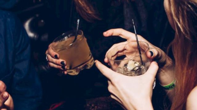 People enjoying drinks and laughing, holding cocktails with straws in a lively social setting.