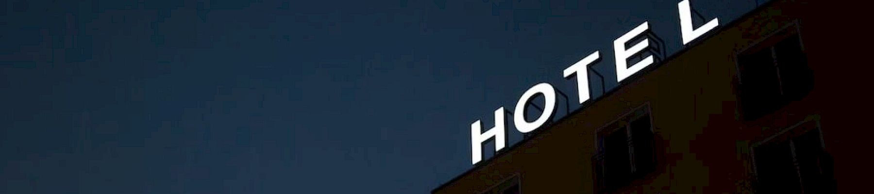 The image shows a building with a sign that reads "HOTEL" at night, with one letter missing, against a dark sky.