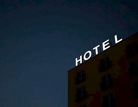 The image shows a building with a sign that reads "HOTEL" at night, with one letter missing, against a dark sky.