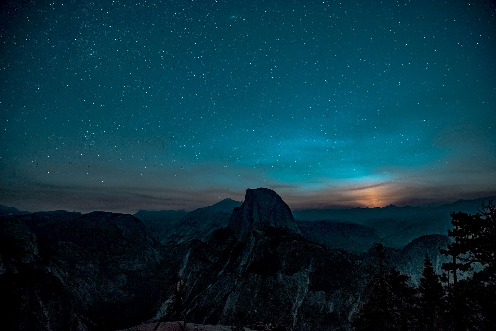A night landscape with a starry sky, a silhouetted mountain, and a glowing horizon, surrounded by dark trees and scenery.