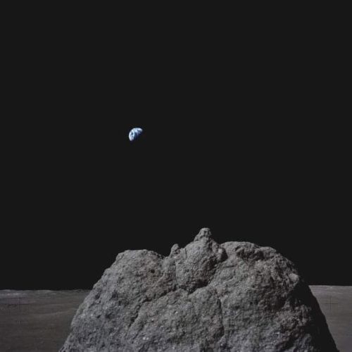 The image shows a view from the Moon's surface with Earth visible in the distance against the dark sky.