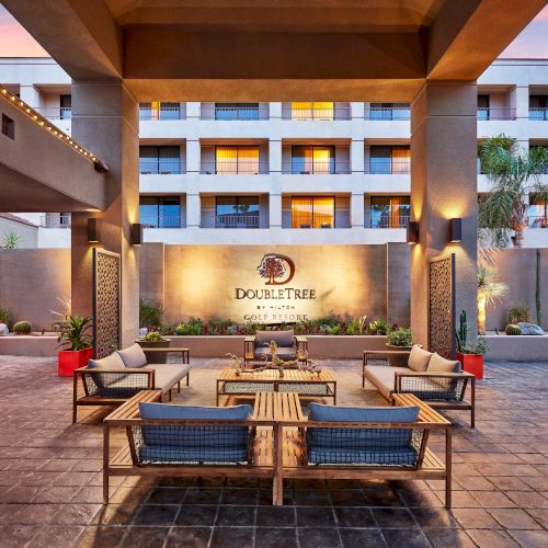 Outdoor seating area at a DoubleTree by Hilton, featuring modern furniture, decorative panels, and plants, under a warm evening sky.