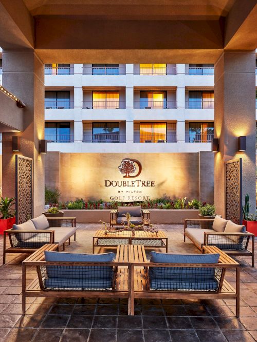 Outdoor seating area at a DoubleTree by Hilton, featuring modern furniture, decorative panels, and plants, under a warm evening sky.
