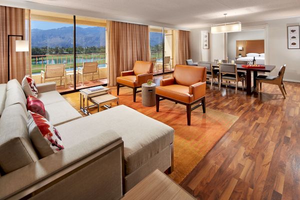 A modern living room with large windows, mountain view, cozy seating, and a dining table, blending comfort with style.
