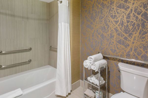 A bathroom with a bathtub, shower curtain, textured wall, toilet, and a stand with neatly rolled towels next to the tub.