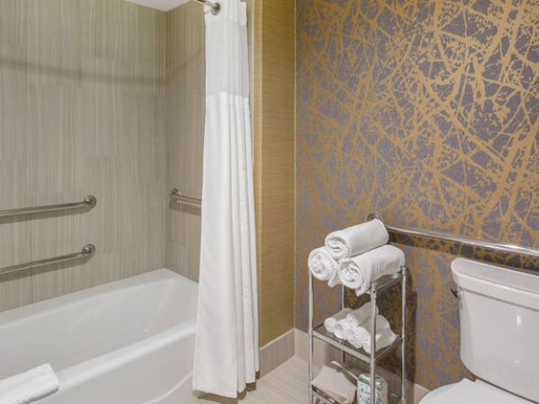 A bathroom with a bathtub, shower curtain, textured wall, toilet, and a stand with neatly rolled towels next to the tub.