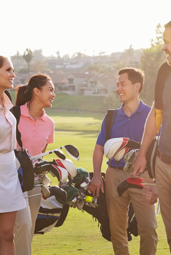 Four people with golf bags smiling and chatting on a sunny golf course.