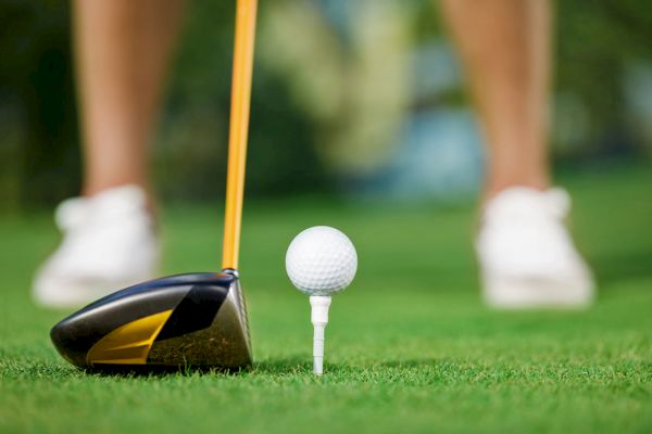 A golf club is poised near a tee with a golf ball on a green field, ready for a swing.
