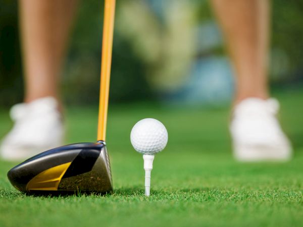 A golf club is poised near a tee with a golf ball on a green field, ready for a swing.