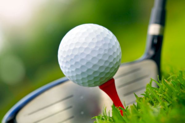 A close-up of a golf ball on a red tee, ready to be hit by a golf club on a green background.