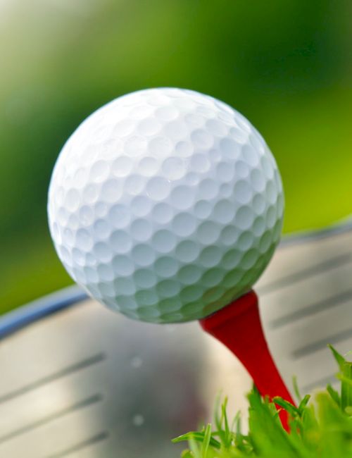 A golf ball on a red tee is positioned in front of a golf club on a grassy area, ready for a shot.