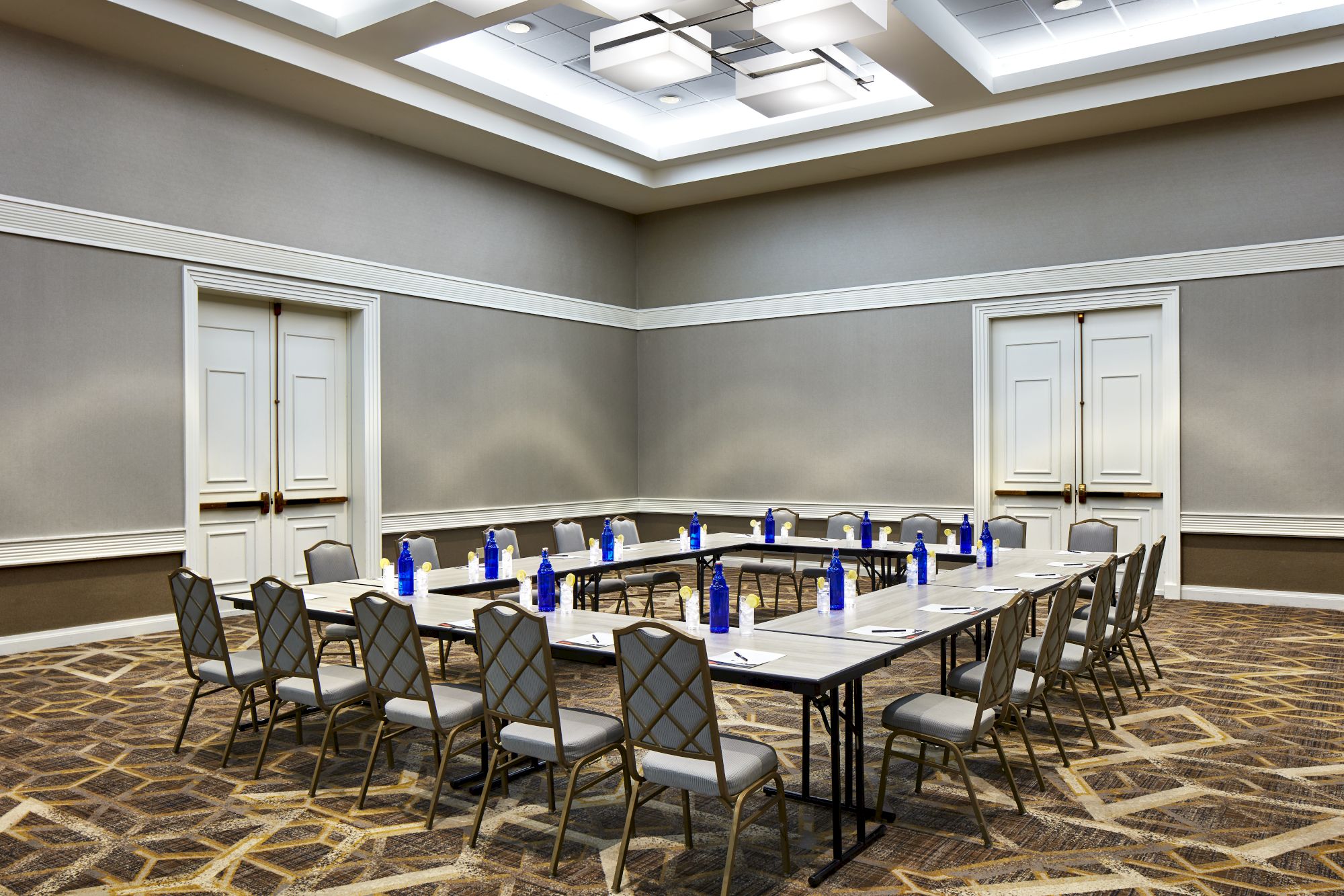 This image shows a conference room with a U-shaped table setup, surrounded by chairs. Water bottles are placed on the tables in the room.