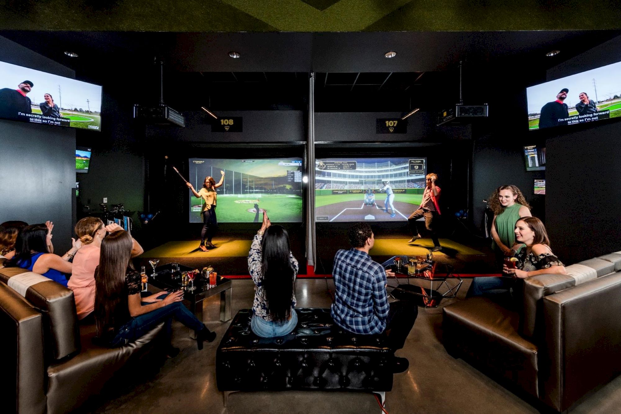 A group of people is enjoying interactive golf simulations, with some playing and others watching, seated in a lounge area.