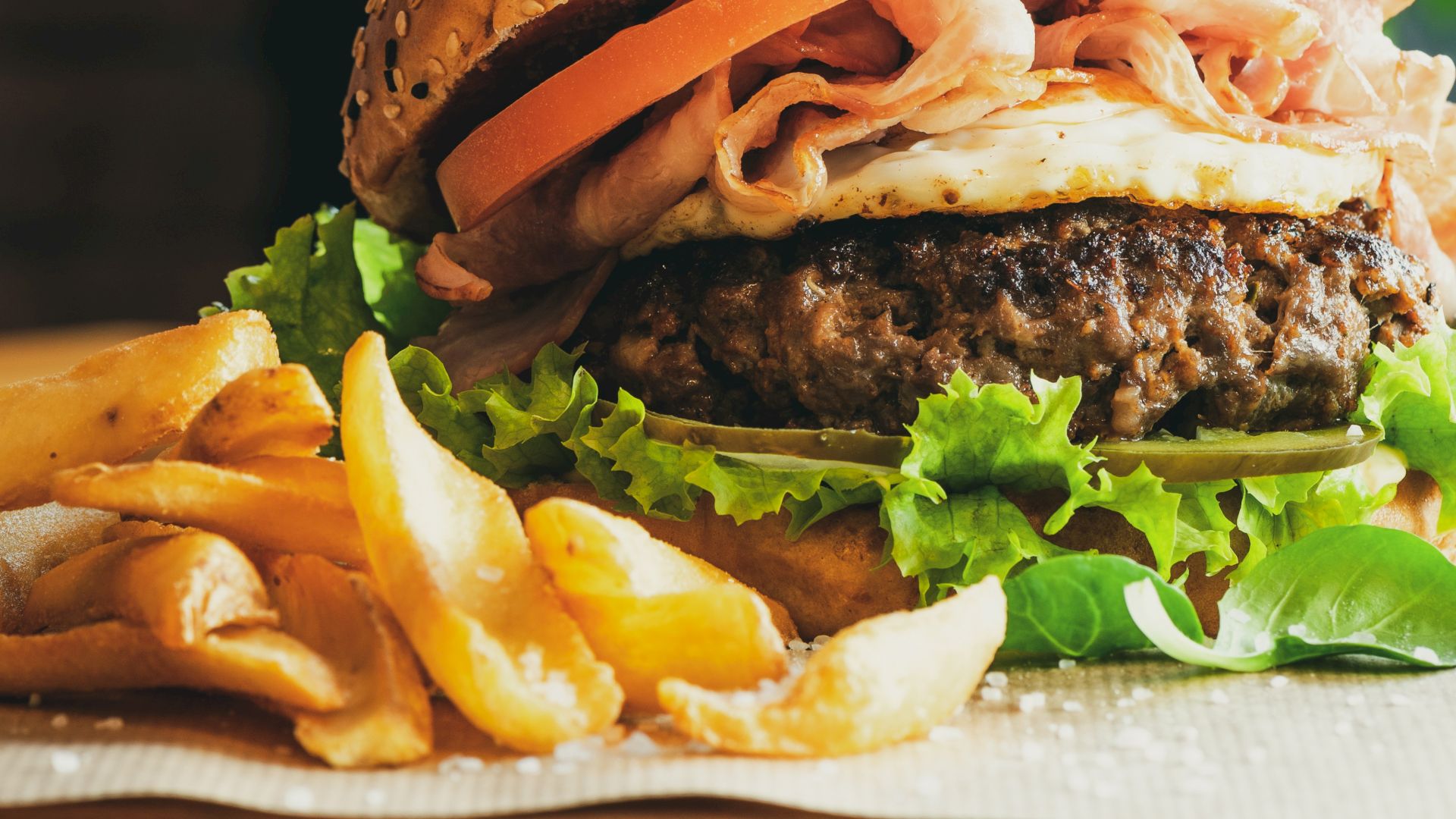 A juicy burger with lettuce, tomato, and roast beef, served with a side of crispy fries on a wooden table.