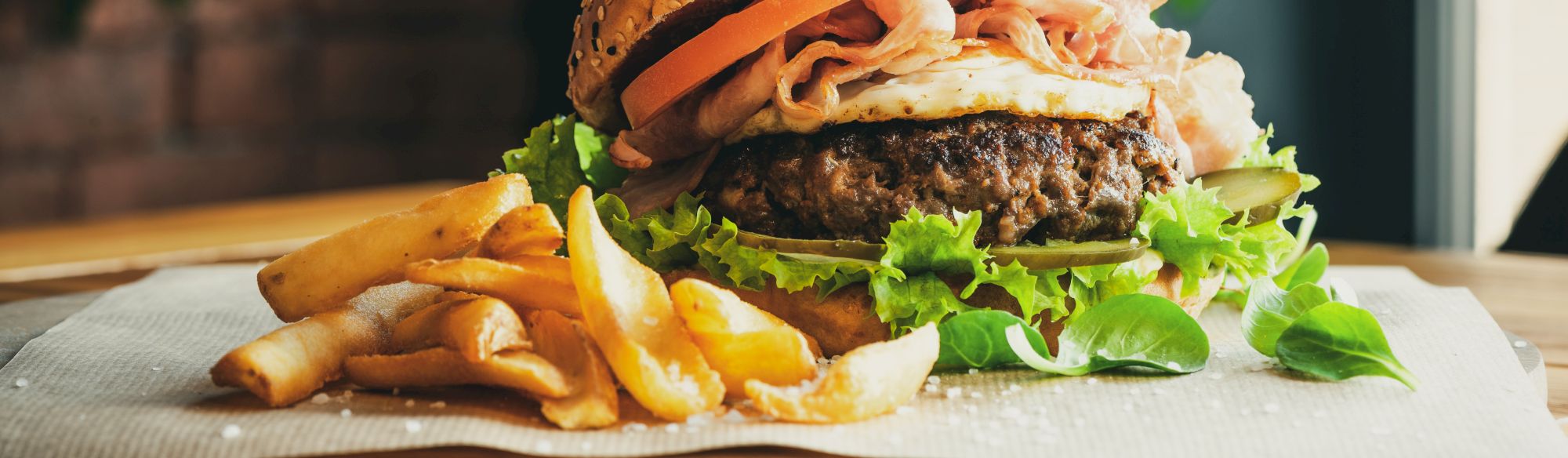 A juicy burger with lettuce, tomato, and roast beef, served with a side of crispy fries on a wooden table.