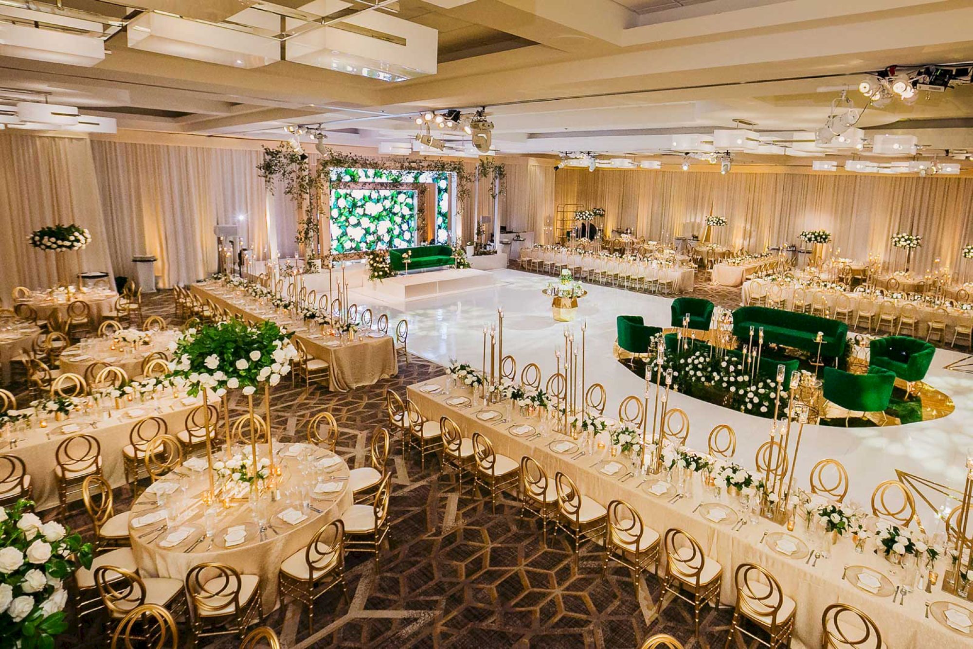 A lavish event hall with elegant table settings, green and gold decor, and a spacious dance floor, ready for a grand celebration.