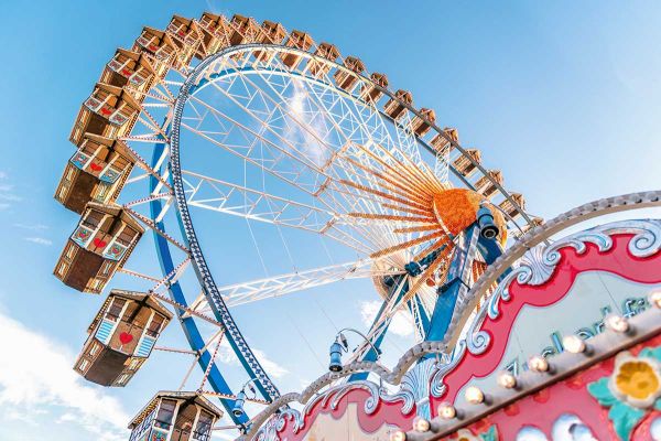 The image shows a colorful Ferris wheel against a clear blue sky, with decorative carnival elements in the foreground.