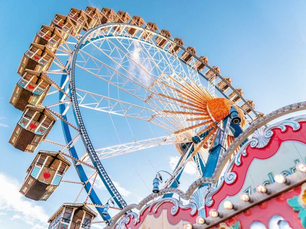 The image shows a colorful Ferris wheel against a clear blue sky, with decorative carnival elements in the foreground.
