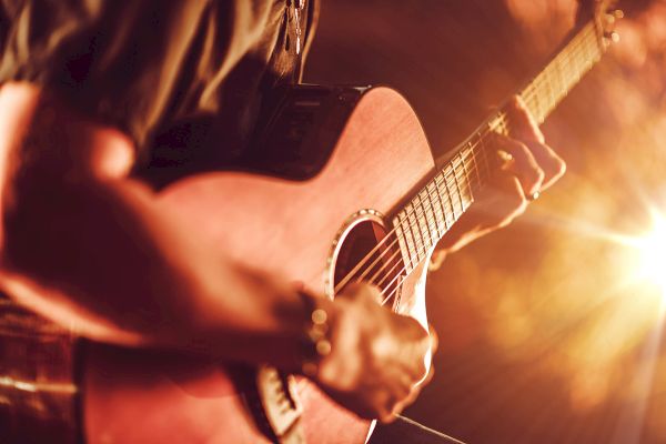 A person is playing an acoustic guitar with a warm light illuminating the scene, creating a cozy, intimate atmosphere.