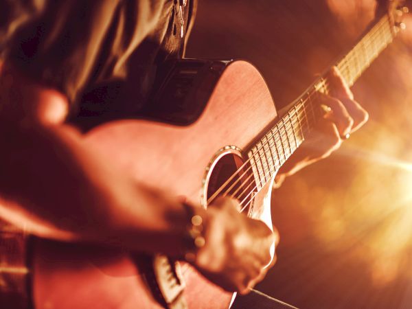 A person is playing an acoustic guitar with a warm light illuminating the scene, creating a cozy, intimate atmosphere.
