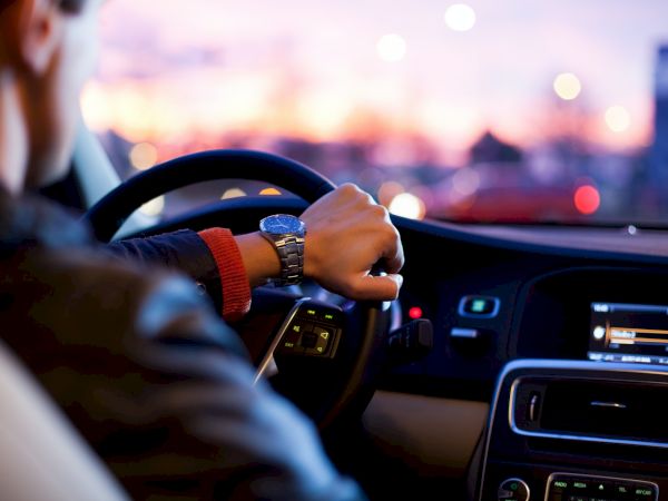 A person is driving a car, with a focus on the steering wheel and dashboard at sunset.
