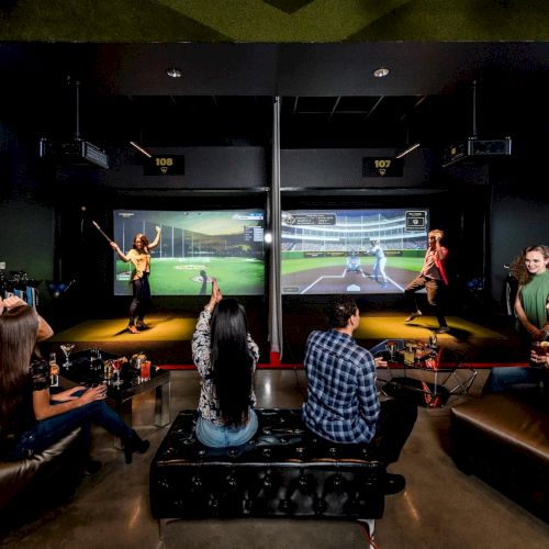 People are in an indoor entertainment venue with sports simulators, golf screens, and seating areas, engaging in activities and socializing.