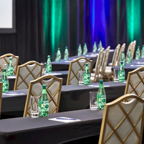 An empty conference room with rows of tables and chairs, bottles of water, notepads, and glasses, set up for a meeting or event.