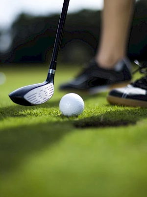 A close-up of a golfer preparing to swing at a golf ball on the grass, with multiple balls visible in the background.