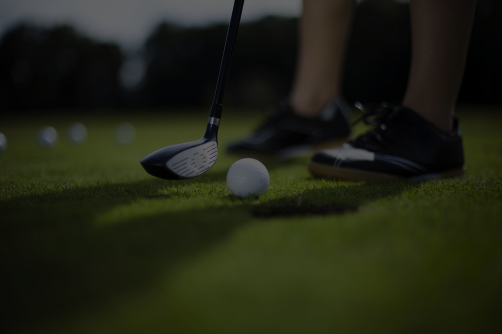 A golf club and a ball on a grassy field, with a person wearing golf shoes standing nearby, prepare for a shot.