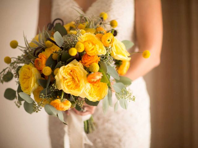 A person holding a vibrant bouquet of yellow and orange flowers with greenery, wearing a lace dress.