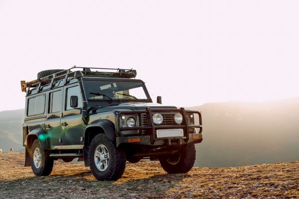 A rugged off-road vehicle is parked on a rocky landscape with a setting sun in the background.