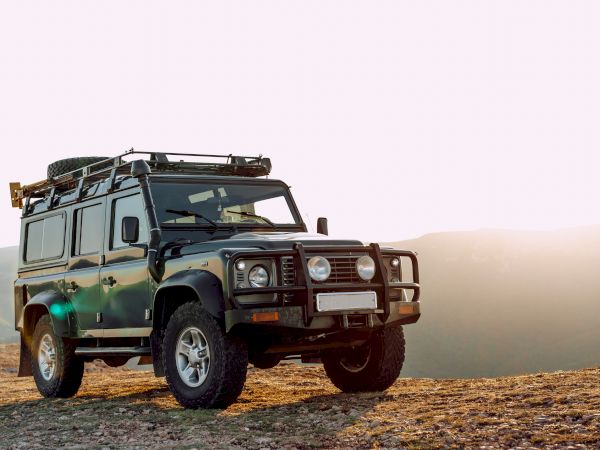 A rugged off-road vehicle is parked on a rocky landscape with a setting sun in the background.