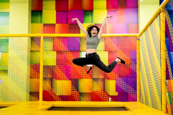 A person is joyfully jumping on a trampoline inside a colorful indoor playground area.