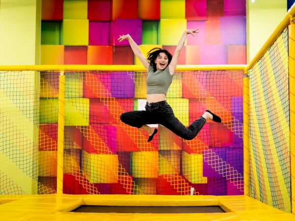 A person is joyfully jumping on a trampoline inside a colorful indoor playground area.