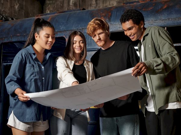 Four people are gathered around, examining a large blueprint, smiling and discussing the details.