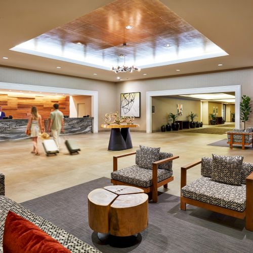 A hotel lobby with modern decor, featuring a reception desk with staff, guests with luggage, and stylish seating areas for relaxation.