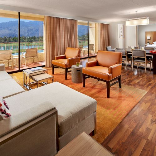 A spacious living room with modern furniture, large windows overlooking a scenic view, and an open dining area in the background.