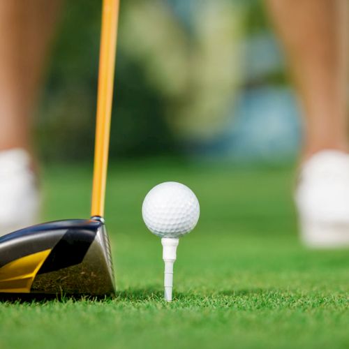 A golf club is positioned near a golf ball on a tee, ready to be struck on a grassy course.