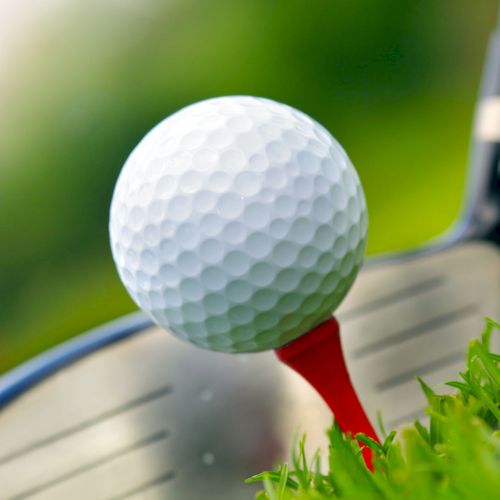 A close-up of a golf ball on a red tee with a golf club poised to hit, set against a grassy background.