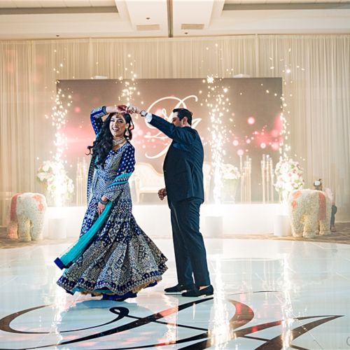 A couple dancing in a decorated venue with sparkler effects, wearing elegant attire.