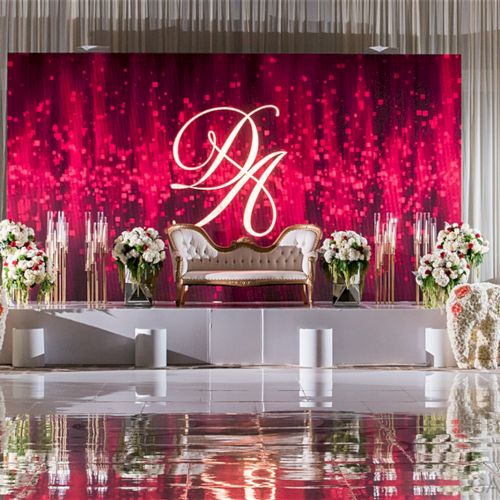 Elegant red stage with initials "DA," featuring a white couch, floral arrangements, and candles, creating a sophisticated setup.