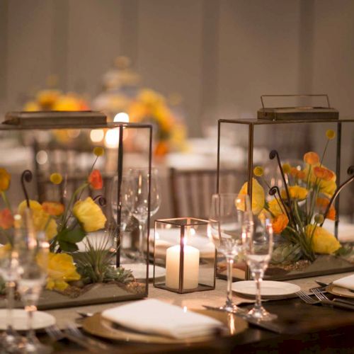 Elegant table setting with glass lanterns, colorful flowers, lit candles, plates, and glassware.