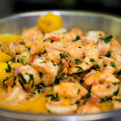 The image shows a dish of shrimp cooked with herbs, garlic, and lemon slices, served in a sauce.